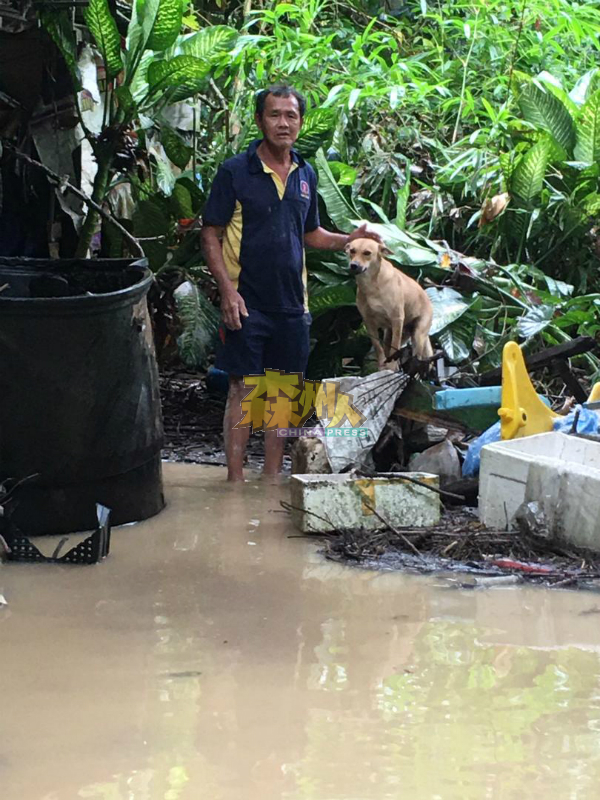 李阿牙与狗一起站在河水淹浸的住家。