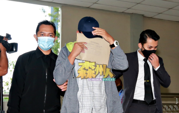 被告阿都哈林（中）发现大批媒体守在庭外，马上向押送他的反贪会官员讨取文件遮脸。