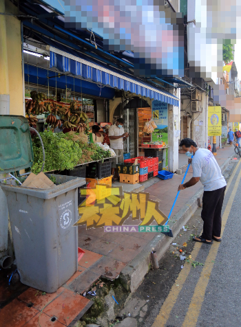 杂货店外的马路上，到处是随手乱丢的各种垃圾，有菜叶、果皮、有废纸、收据，业者被执法员下令赶快清理。