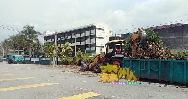 挖泥机在学校门外把废弃木质物移到垃圾槽。