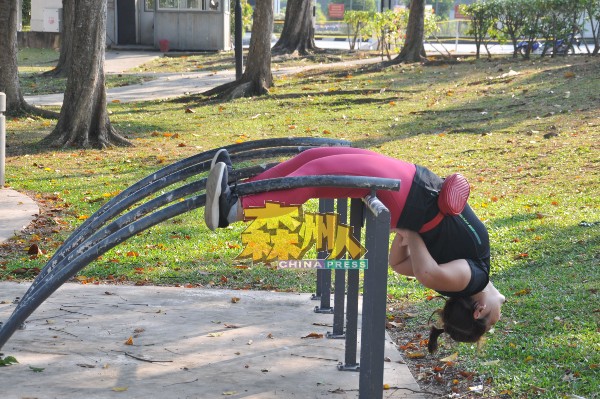 一名妇女借助公园的设备，展开高难度的拉筋动作。