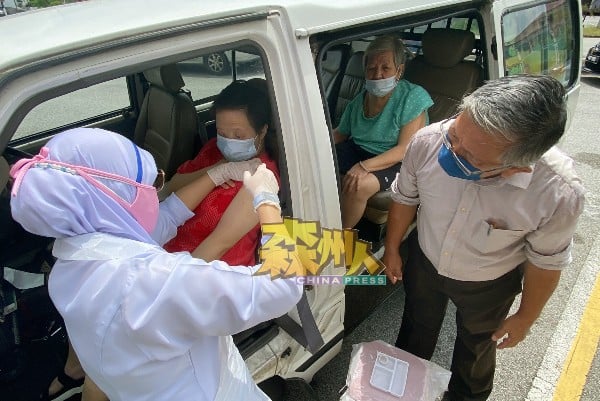 从吉隆坡下来的医护人员西蒂，亲自到车旁细心为行动不便的81岁长者（车后）和残疾患者（车前）施打疫苗，周世扬（右）在旁给予安抚，场面温馨。