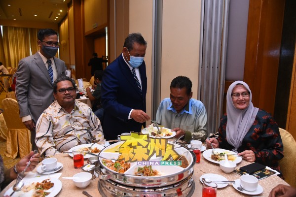 阿米努丁（站者右）在主持仪式后，走入宴席间与退休公务员交流，还亲自舀食物给出席者。