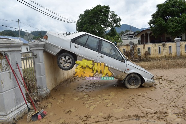 其中一辆轿车被洪水冲至悬挂在围墙上。