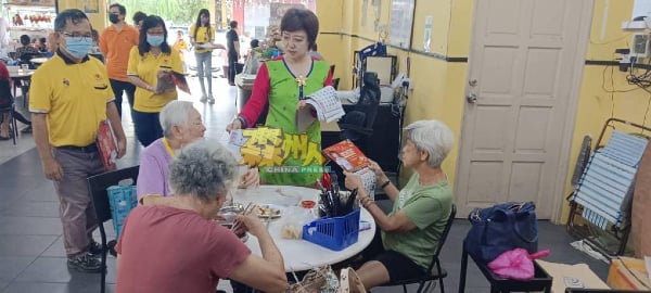 陈丽群（站者右）到芙蓉新城城市公园的商业区派发月历给民众。