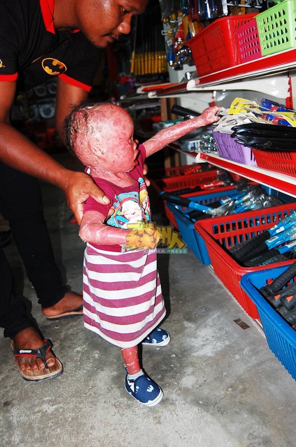 两岁的迪亚拉站不稳，也不会步行，父亲阿兹兰扶着她逛五金店。