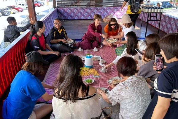 东北旅游考察团的团员，学习如何席地而坐享用马来传统美食。