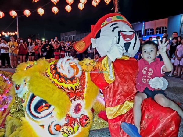 神情失措孩童临危不乱的让财神爷抱着，跟着瑞狮向市民拜年。