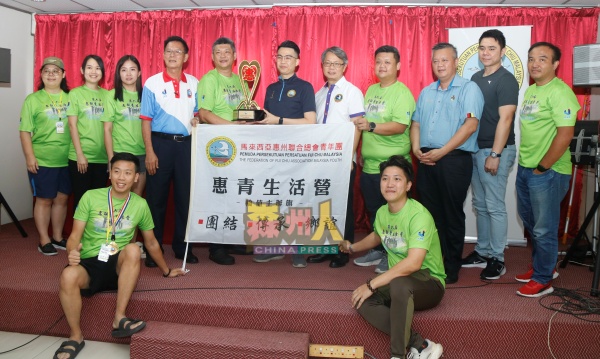 在众嘉宾见证下,萧国栓(站者左5起)将“惠青生活营”旗帜与奖座交予彭俊达接棒,左起为吴心怡、潘颖珊、欧阳凯丝、黄俊棠、刘志荣、陈友祥、吴金财、卜伟光、魏国明,前排坐者左起为雷顺安、武键辉。
